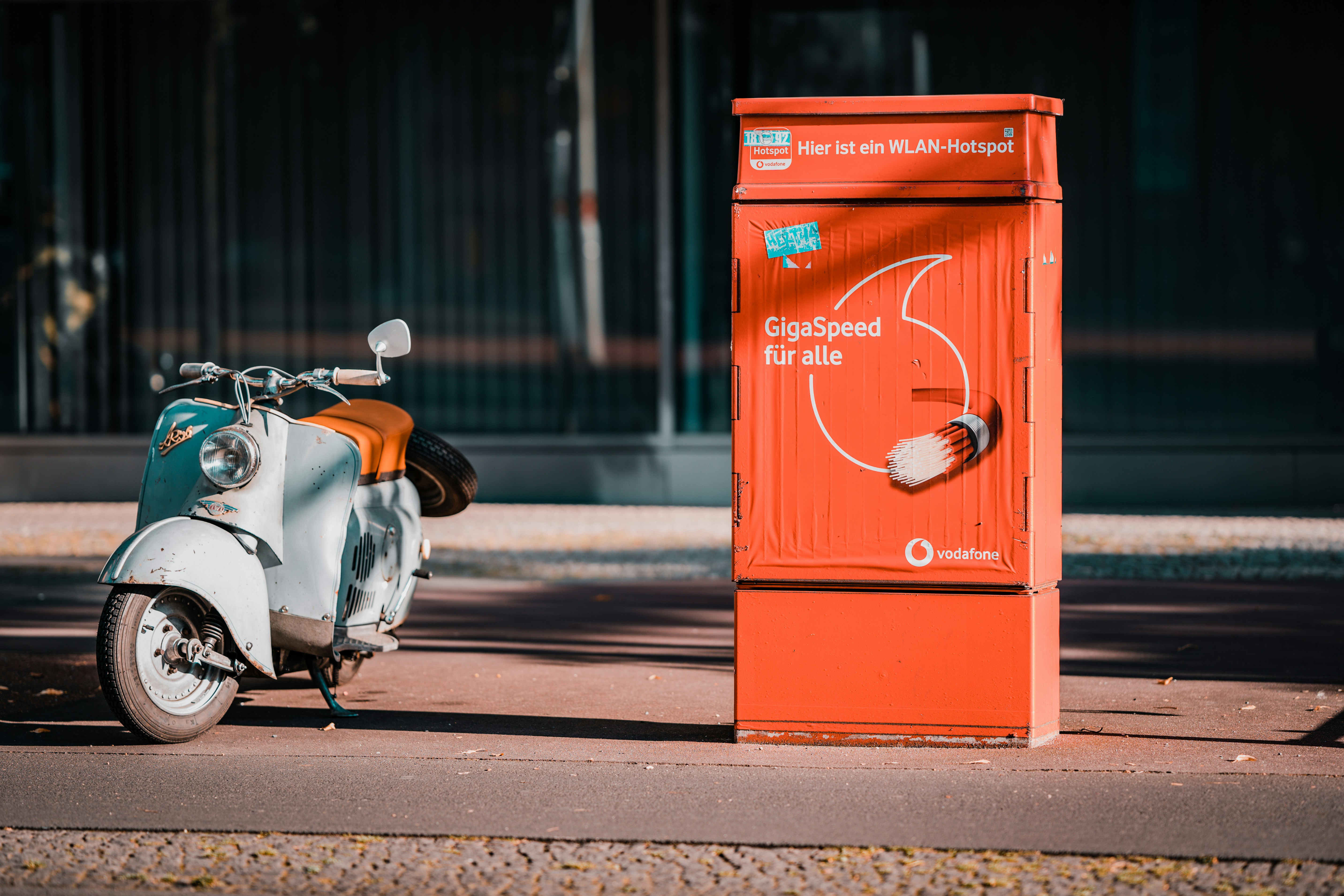 red and white motor scooter parked beside red steel gate during daytime